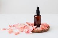 pexels photo 4041386 4041386 Gentle pale pink wavy rose petals placed on small round wooden plate and table near dark glass essence flask on white background